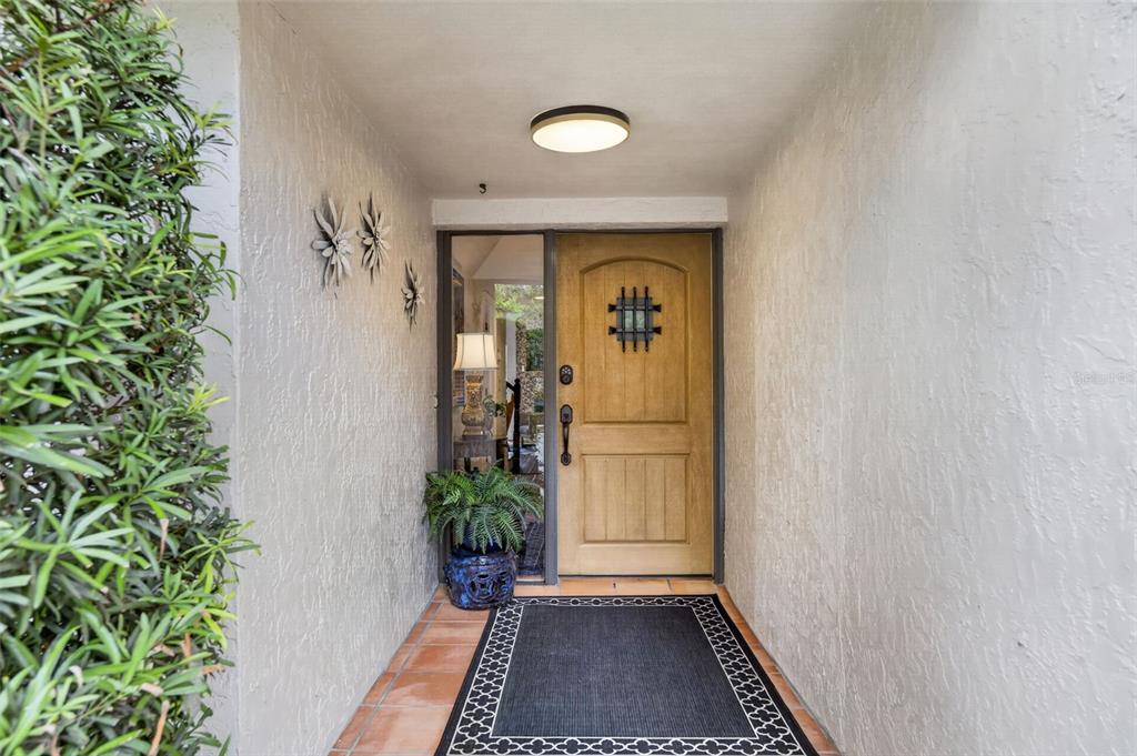An exterior entryway features a wooden door with a decorative grille, tile flooring, and greenery — 2881 TEMPLE TRAIL, WINTER PARK, FL