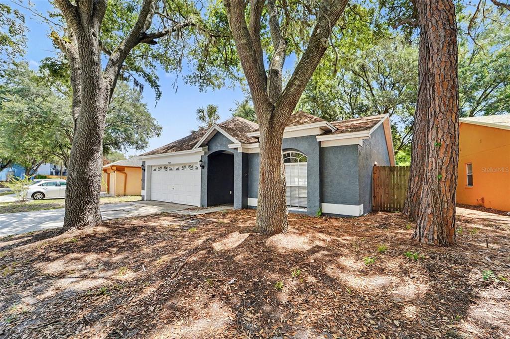 A gray single-story house with a white garage door sits among large trees — 7603 SAVANNAH LANE, TAMPA, FL