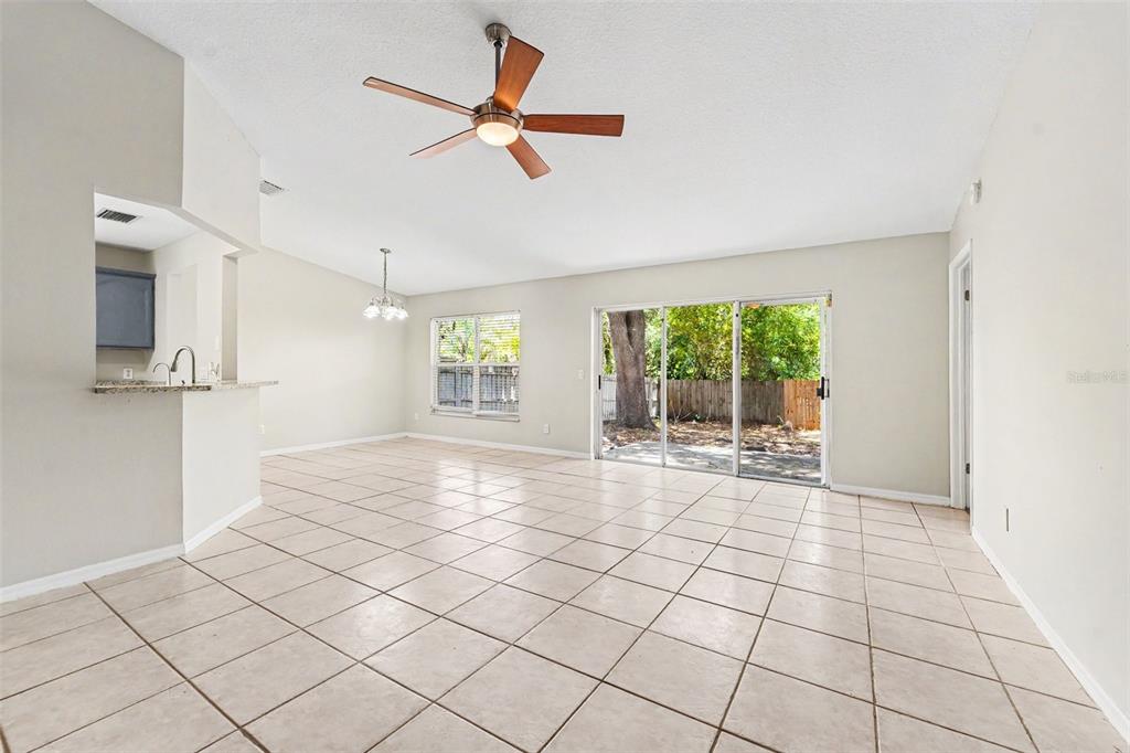 A spacious living room features light tile flooring, a ceiling fan, and sliding glass doors — 7603 SAVANNAH LANE, TAMPA, FL