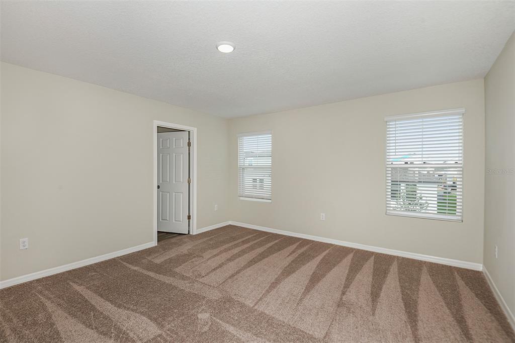 An empty bedroom features beige walls, brown carpet, two windows with blinds, and a door — 1719 VANILLA STREET, HAINES CITY, FL