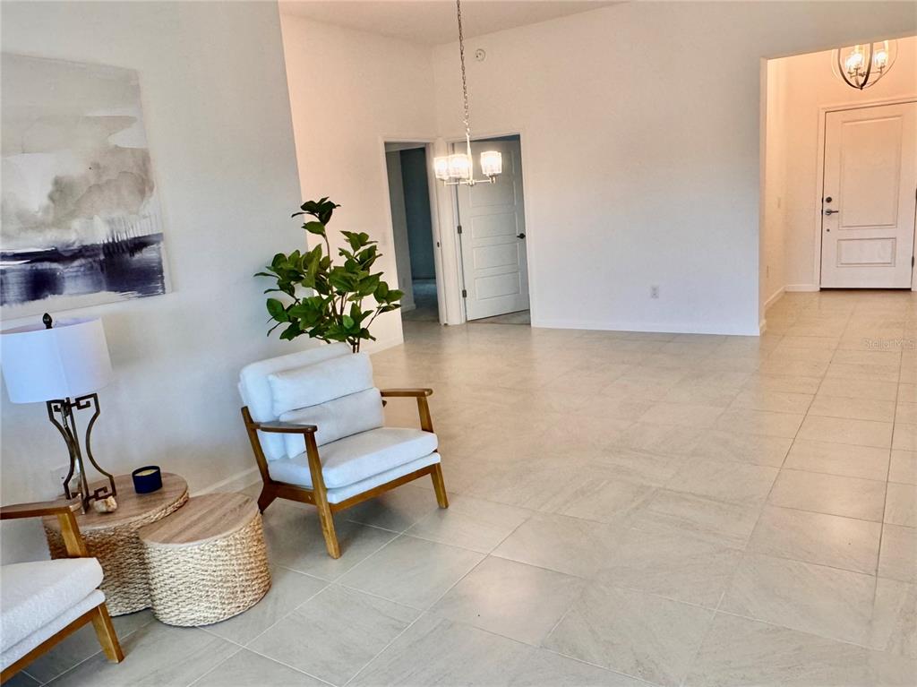 A bright, open-concept living area features light tile flooring, a white armchair, and a chandelier — 1454 JEREMY CIRCLE, THE VILLAGES, FL
