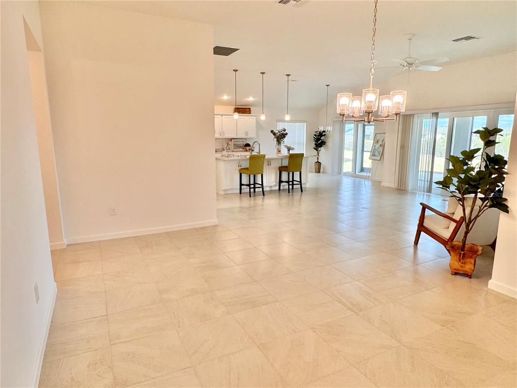 An open-concept living and kitchen area features light tile flooring and a chandelier — 1454 JEREMY CIRCLE, THE VILLAGES, FL