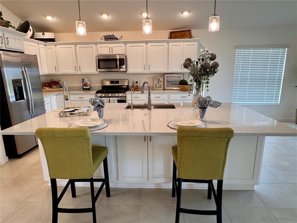A kitchen features white cabinets, stainless steel appliances, a large island, and two green chairs — 1454 JEREMY CIRCLE, THE VILLAGES, FL