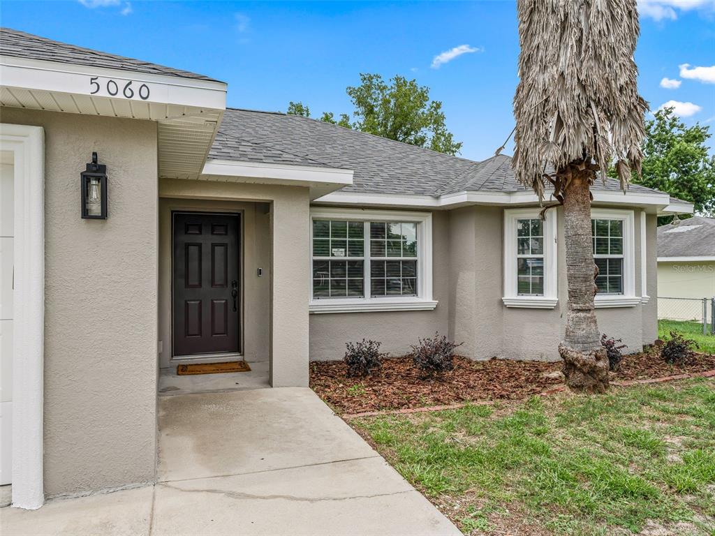 The exterior of a single-story house features a tan stucco facade, a dark front door, and a palm tree — 5060 PECAN ROAD, OCALA, FL