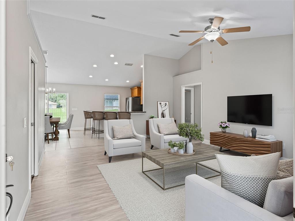 A bright, open-concept living room features light wood-look flooring, a vaulted ceiling, and neutral decor — 5060 PECAN ROAD, OCALA, FL