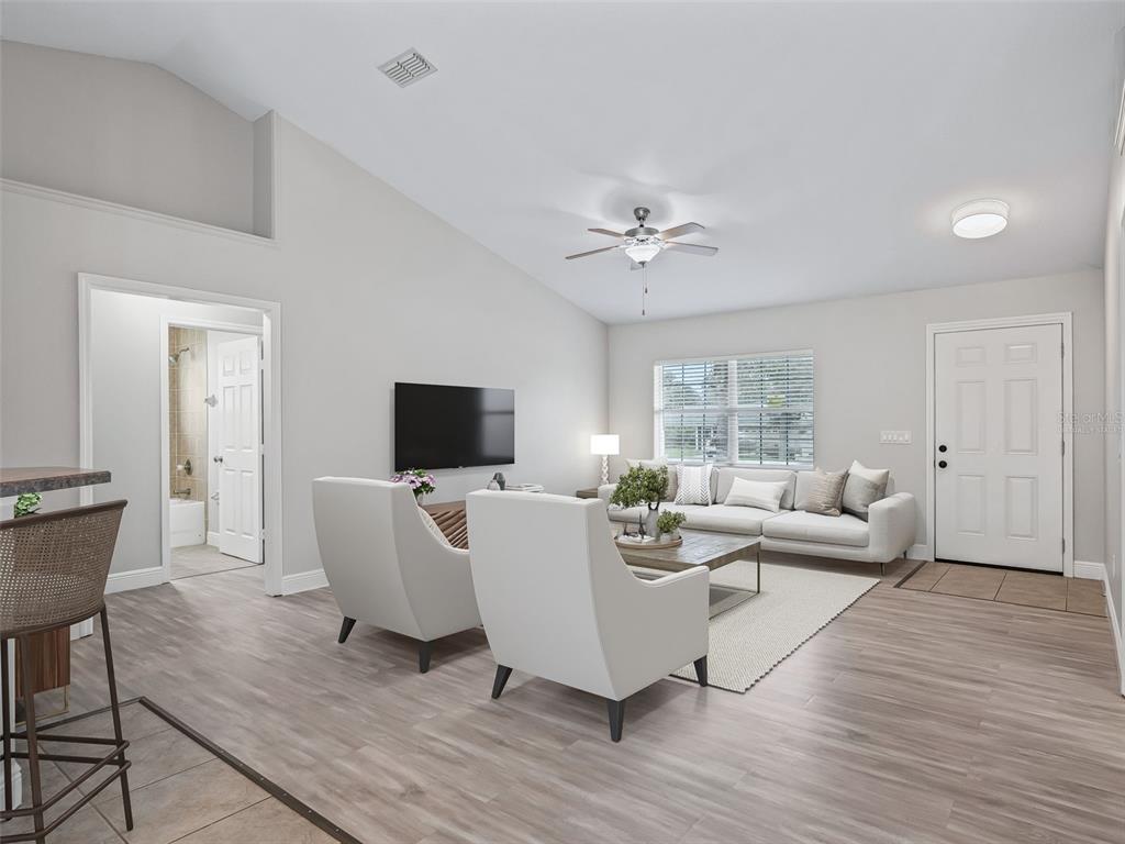 A living room features light gray walls, wood-look flooring, a vaulted ceiling, and white furniture — 5060 PECAN ROAD, OCALA, FL