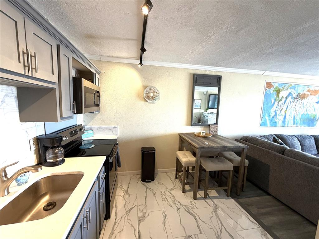 A kitchen features gray cabinets, white marble-look tile flooring, and a small wooden dining set — 51 ISLAND WAY UNIT 705, CLEARWATER BEACH, FL