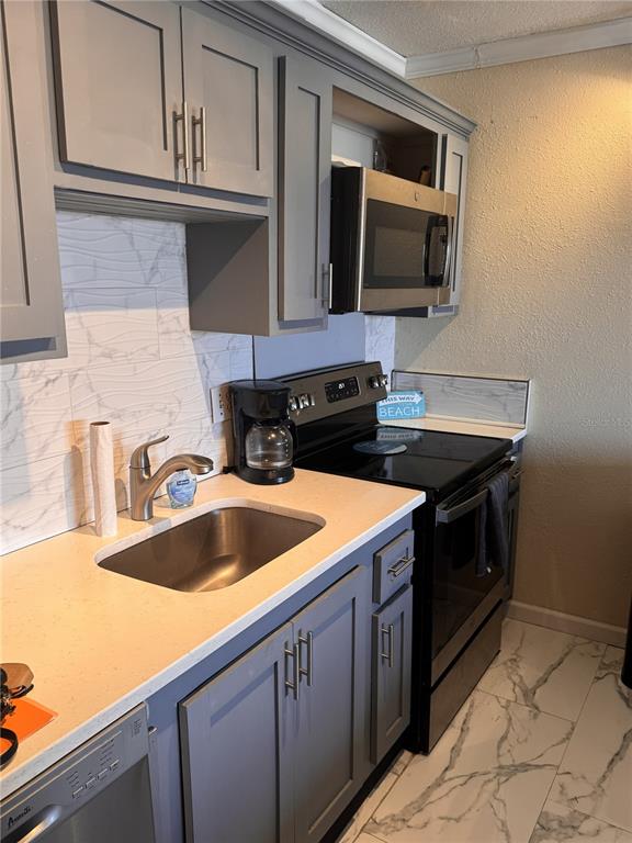 A kitchen features gray cabinets, a stainless steel sink, a black stove, and marble-patterned tile — 51 ISLAND WAY UNIT 705, CLEARWATER BEACH, FL