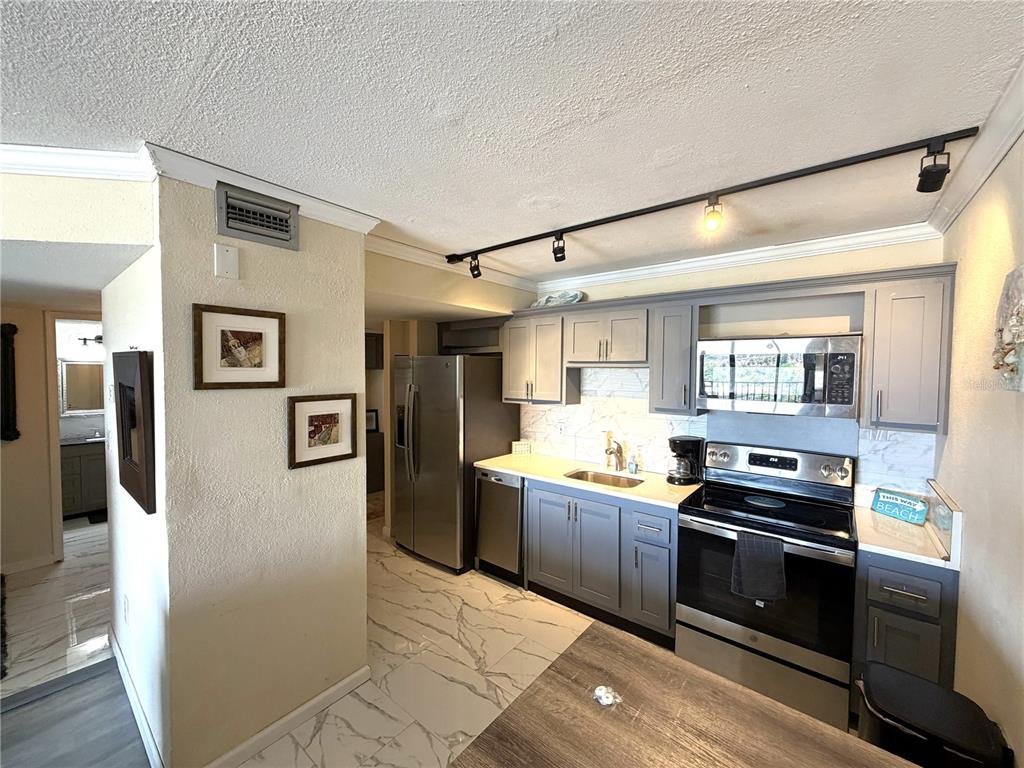 A kitchen features gray cabinets, stainless steel appliances, and white marble-patterned tile flooring — 51 ISLAND WAY UNIT 705, CLEARWATER BEACH, FL