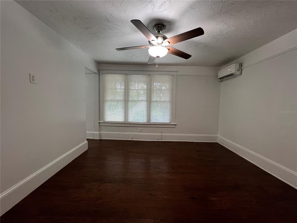 A room with dark hardwood floors, white walls, a ceiling fan, and a wall-mounted air conditioner — 510 E JACKSON ST UNIT 5, ORLANDO, FL