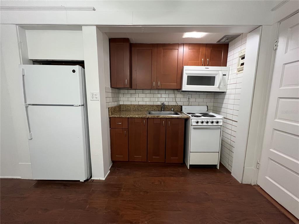 A small kitchen features dark wood cabinets, granite countertops, a white stove, and a refrigerator — 510 E JACKSON ST UNIT 5, ORLANDO, FL