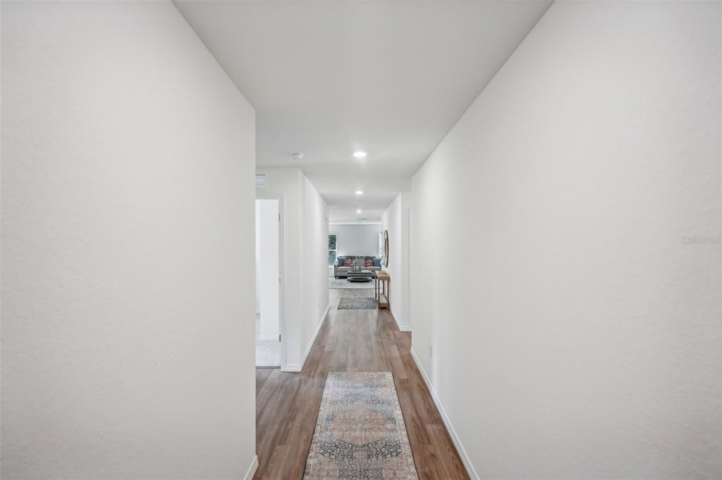 A long hallway with wood-look flooring leads to a living area with a sofa — 5526 CASTINIA DRIVE, SEBRING, FL