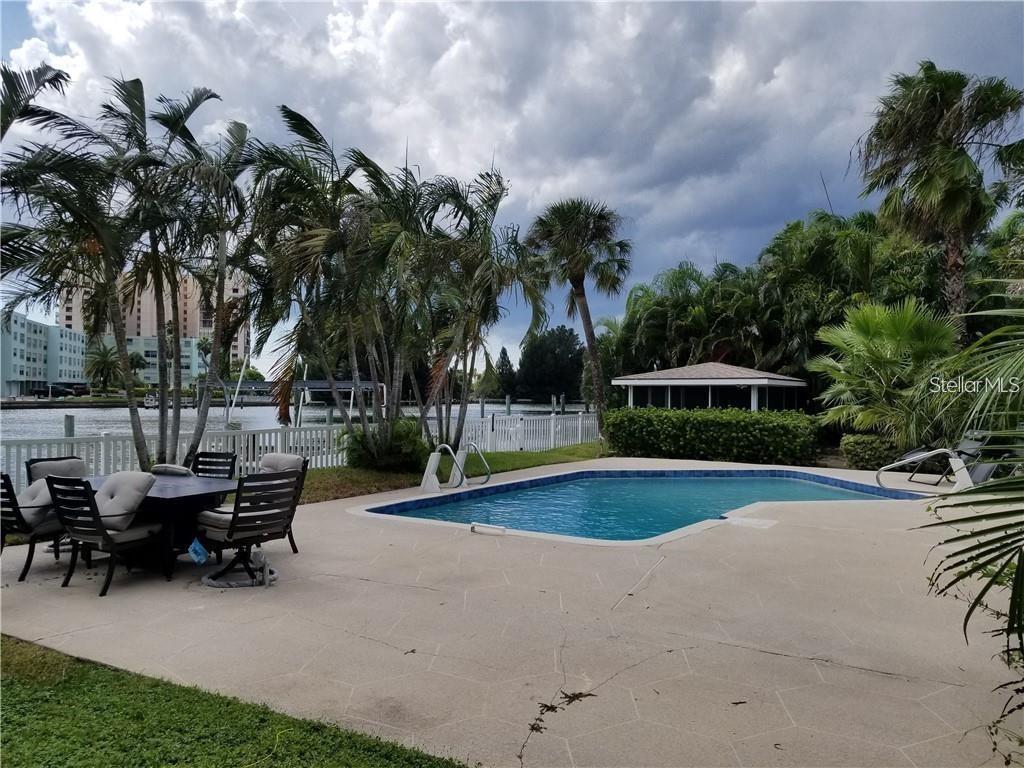 A swimming pool sits on a concrete patio beside a canal with palm trees — 4000 BELLE VISTA DRIVE, ST PETERSBURG, FL