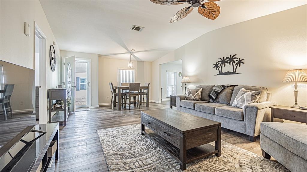 A living room and dining area feature gray wood-look flooring, a gray sofa, and ceiling fans — 37436 LILLY BEA AVENUE, ZEPHYRHILLS, FL