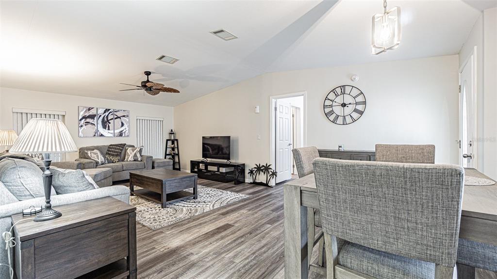 An open-concept living and dining area features wood-look flooring, neutral walls, and modern furniture — 37436 LILLY BEA AVENUE, ZEPHYRHILLS, FL