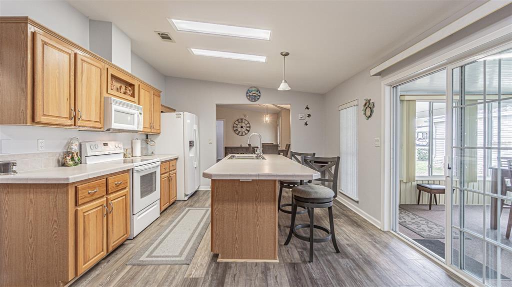 A kitchen with wood cabinets, a central island, and a sliding glass door to a sunroom — 37436 LILLY BEA AVENUE, ZEPHYRHILLS, FL