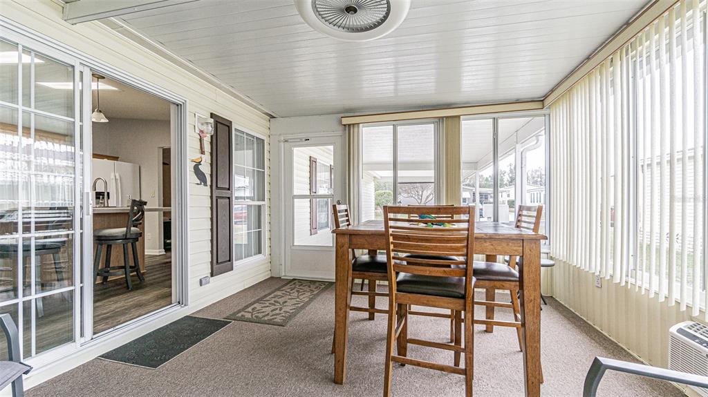 A sunroom features a dining table, carpeted flooring, a ceiling fan, and sliding glass doors — 37436 LILLY BEA AVENUE, ZEPHYRHILLS, FL