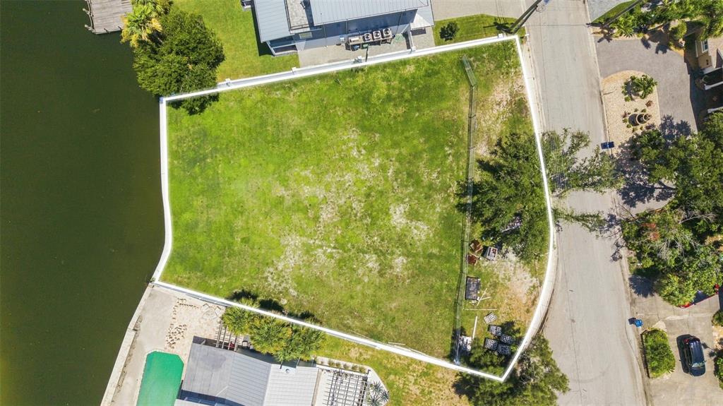 An aerial view shows a vacant, fenced waterfront lot bordered by a road and houses — 5833 MARINER STREET, TAMPA, FL