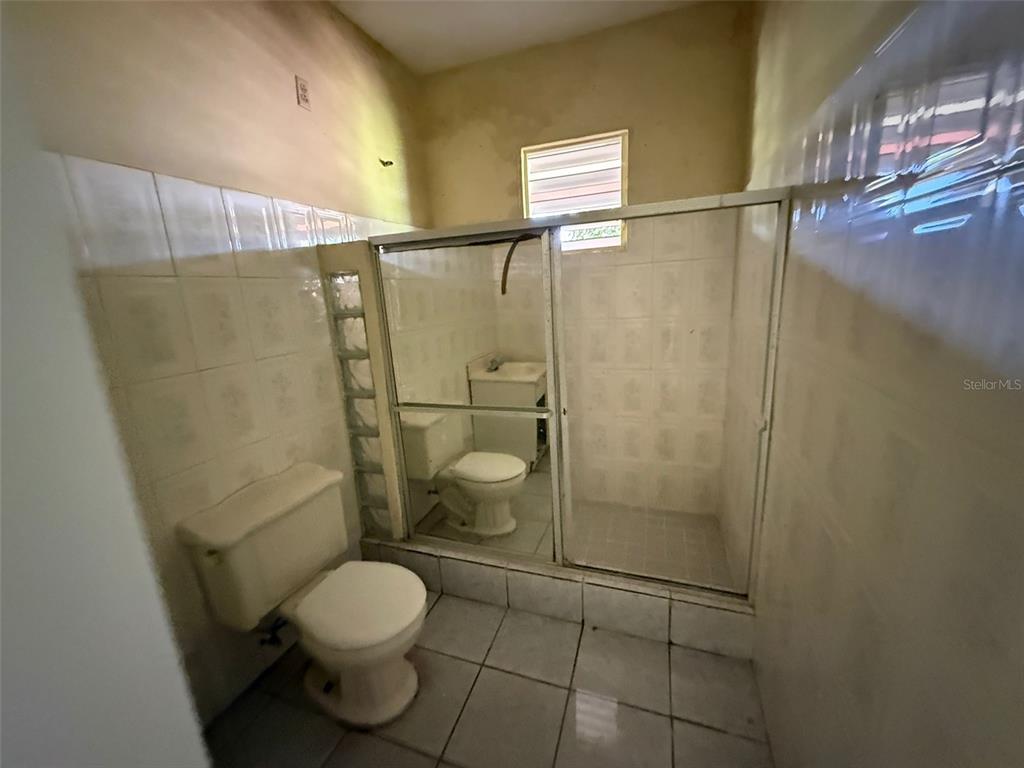 A bathroom features a toilet, a glass-enclosed shower, and white tiled walls and floors — Bo Anones CARR 108, KM. 19.4, LAS MARIAS, PR
