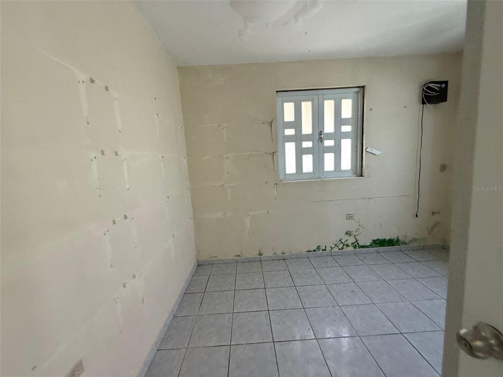 An empty room with tiled floors, a window with security bars, and visible wall damage — Bo Anones CARR 108, KM. 19.4, LAS MARIAS, PR