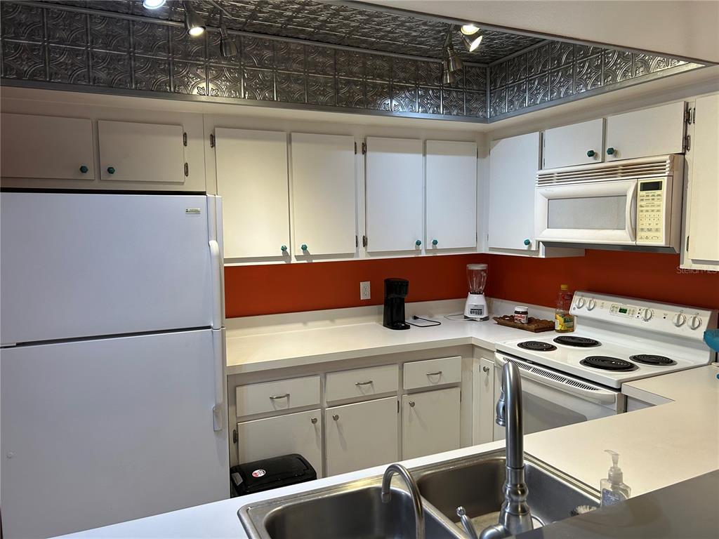 A kitchen features white cabinets, a burnt orange backsplash, and a decorative metallic ceiling panel — 6102 7TH AVENUE W UNIT 6102, BRADENTON, FL