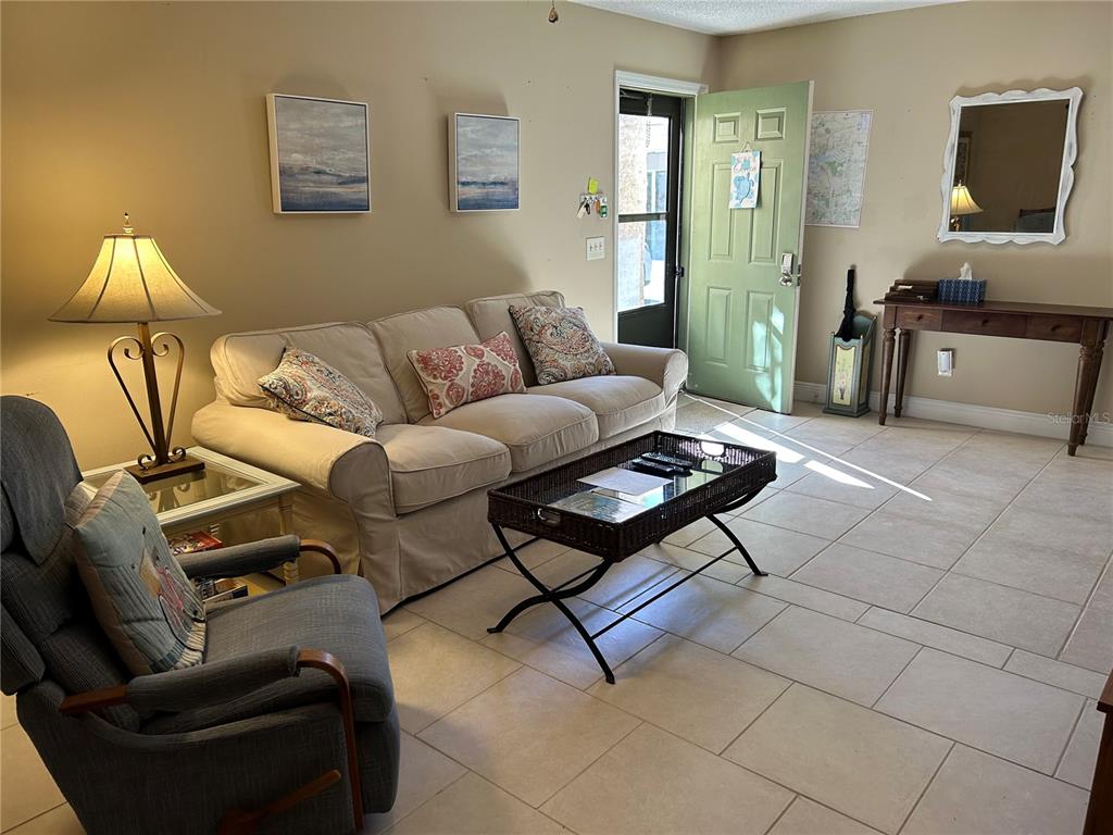 A living room features a beige sofa, a gray armchair, a coffee table, and a green door — 6102 7TH AVENUE W UNIT 6102, BRADENTON, FL