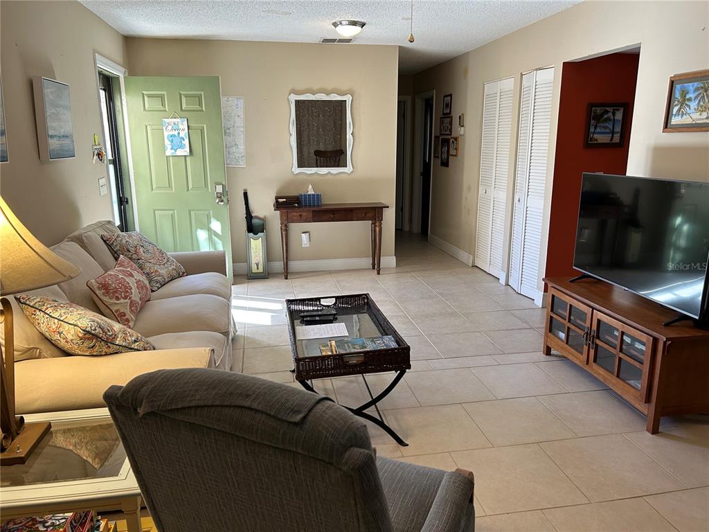 A living room features tile flooring, a beige sofa, a coffee table, and a television — 6102 7TH AVENUE W UNIT 6102, BRADENTON, FL