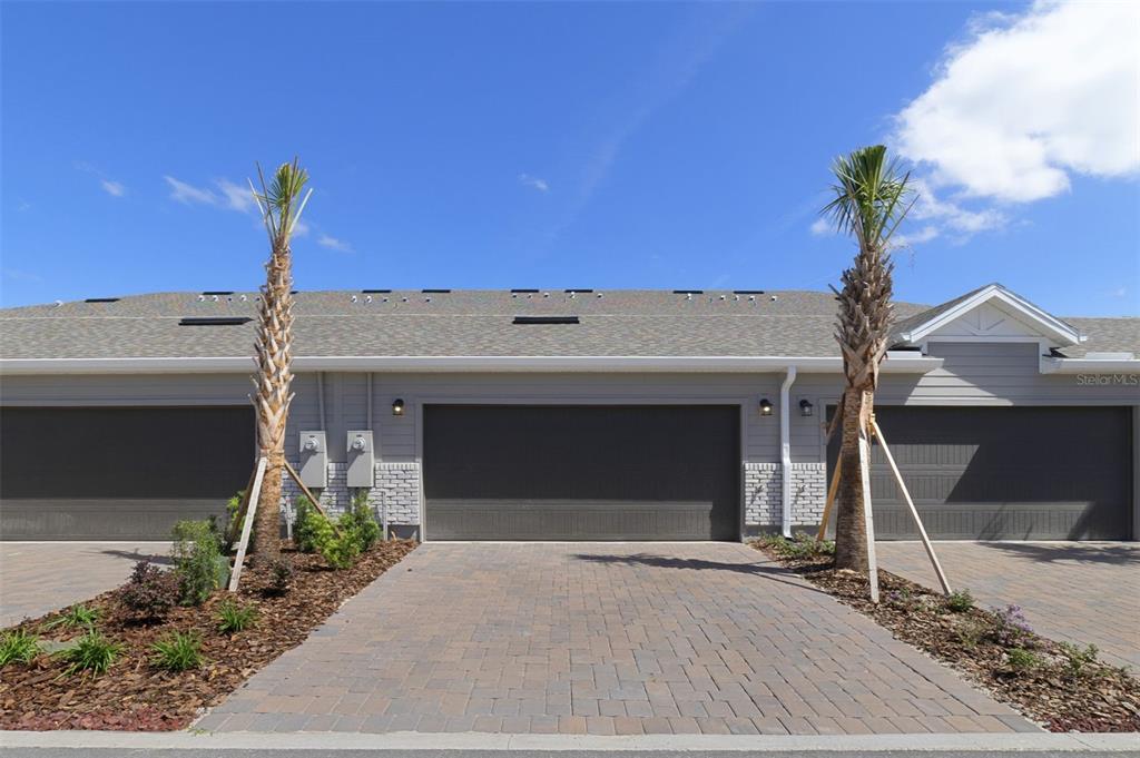 A row of three gray garage doors with paver driveways and palm trees in front — 684 LOLA LANE, OVIEDO, FL