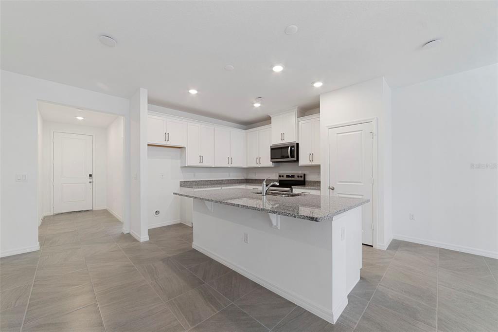 A modern kitchen features white cabinets, granite countertops, a central island, and gray tile flooring — 684 LOLA LANE, OVIEDO, FL