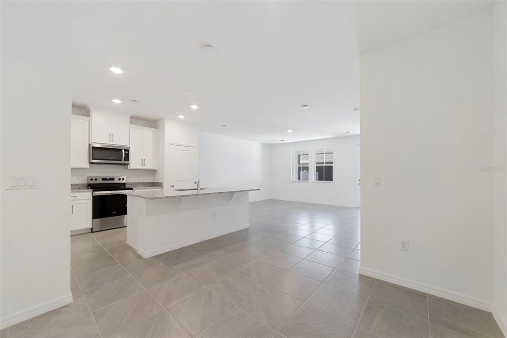 A kitchen with white cabinets and a center island opens into a tiled living area — 684 LOLA LANE, OVIEDO, FL