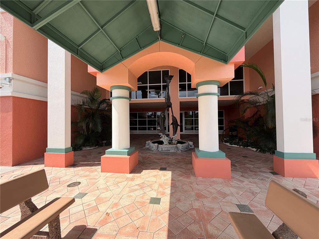 An outdoor covered entrance features a dolphin fountain, tiled flooring, and two benches — 4516 SEAGULL DRIVE UNIT 515, NEW PORT RICHEY, FL