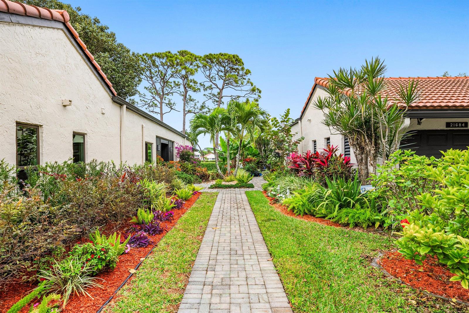 A brick walkway leads between two stucco houses surrounded by lush tropical landscaping — 21680 Tall Palm Circle # B, Boca Raton FL 33433, BOCA RATON, FL