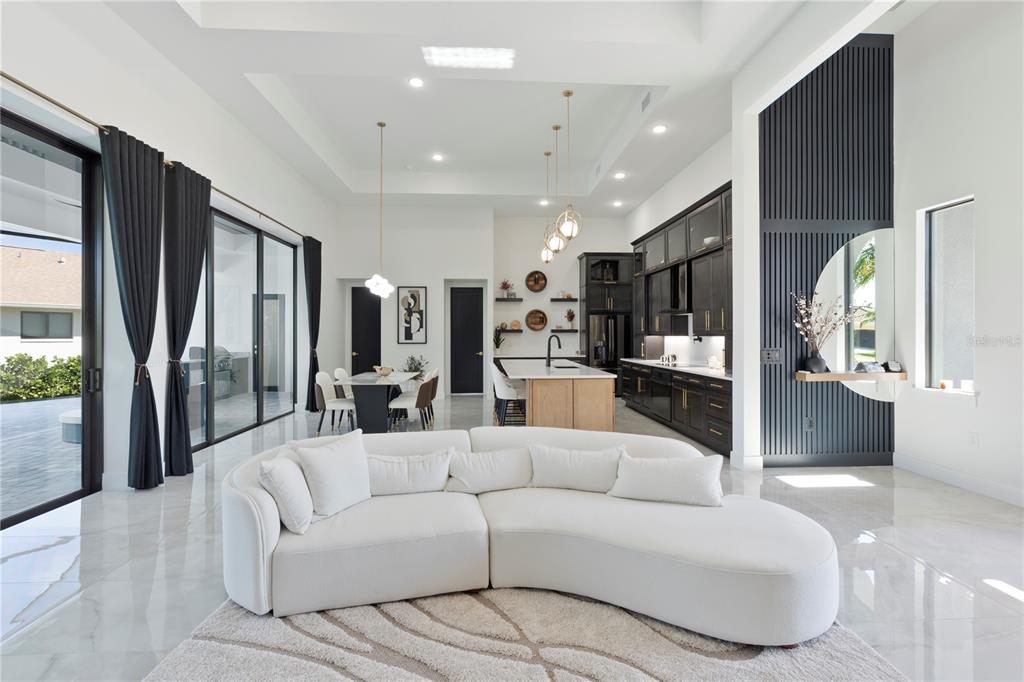 A modern open-concept living room and kitchen feature white tile floors and dark cabinetry — 4218 SW 17TH AVENUE, CAPE CORAL, FL