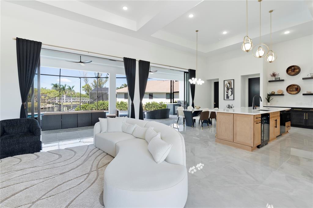 An open-concept living room and kitchen with white tile floors, a curved sofa, and sliding doors — 4218 SW 17TH AVENUE, CAPE CORAL, FL