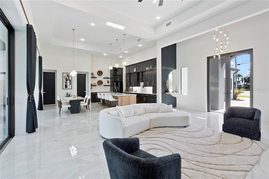 A bright, open-concept living room and kitchen featuring white marble floors and dark cabinetry — 4218 SW 17TH AVENUE, CAPE CORAL, FL