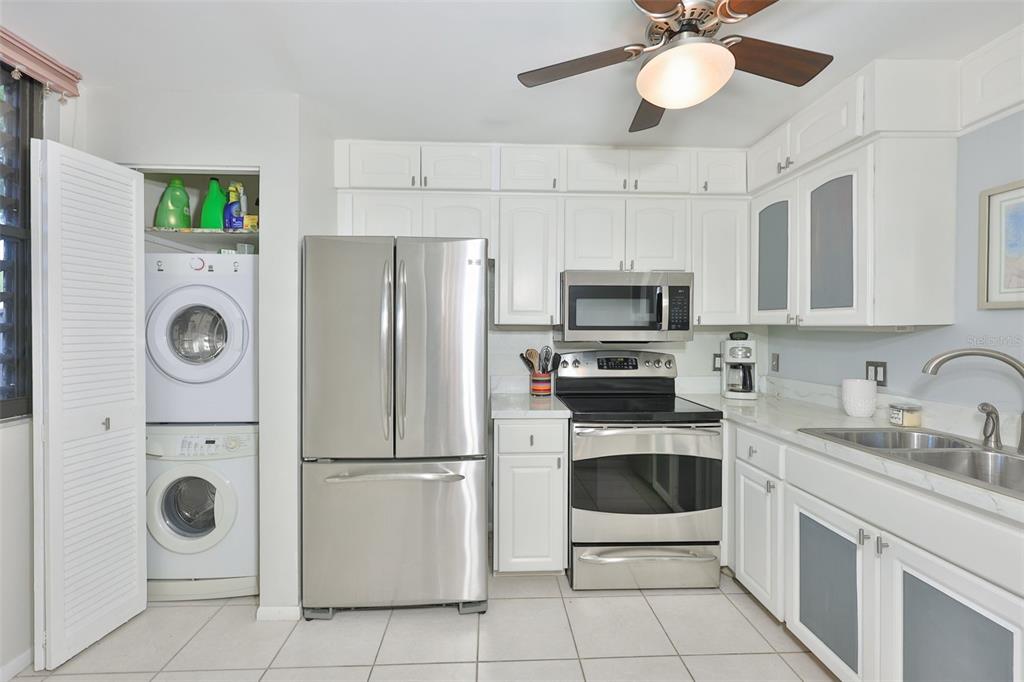 A kitchen features white cabinets, stainless steel appliances, and a stacked washer and dryer unit — 647 WOODLAWN DRIVE UNIT 647, BRADENTON, FL