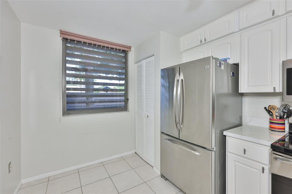 A kitchen features white cabinets, a stainless steel refrigerator, tiled floors, and a window — 647 WOODLAWN DRIVE UNIT 647, BRADENTON, FL