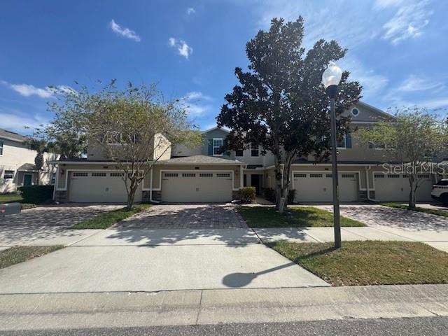 A multi-unit residential building with beige siding, multiple garage doors, and a street lamp — 1221 PRIORY CIRCLE, WINTER GARDEN, FL