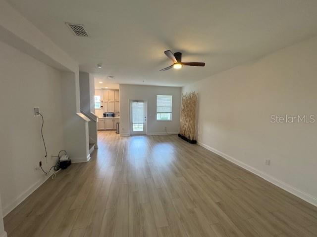 A spacious living room features light wood-look flooring, a ceiling fan, and a staircase — 1221 PRIORY CIRCLE, WINTER GARDEN, FL