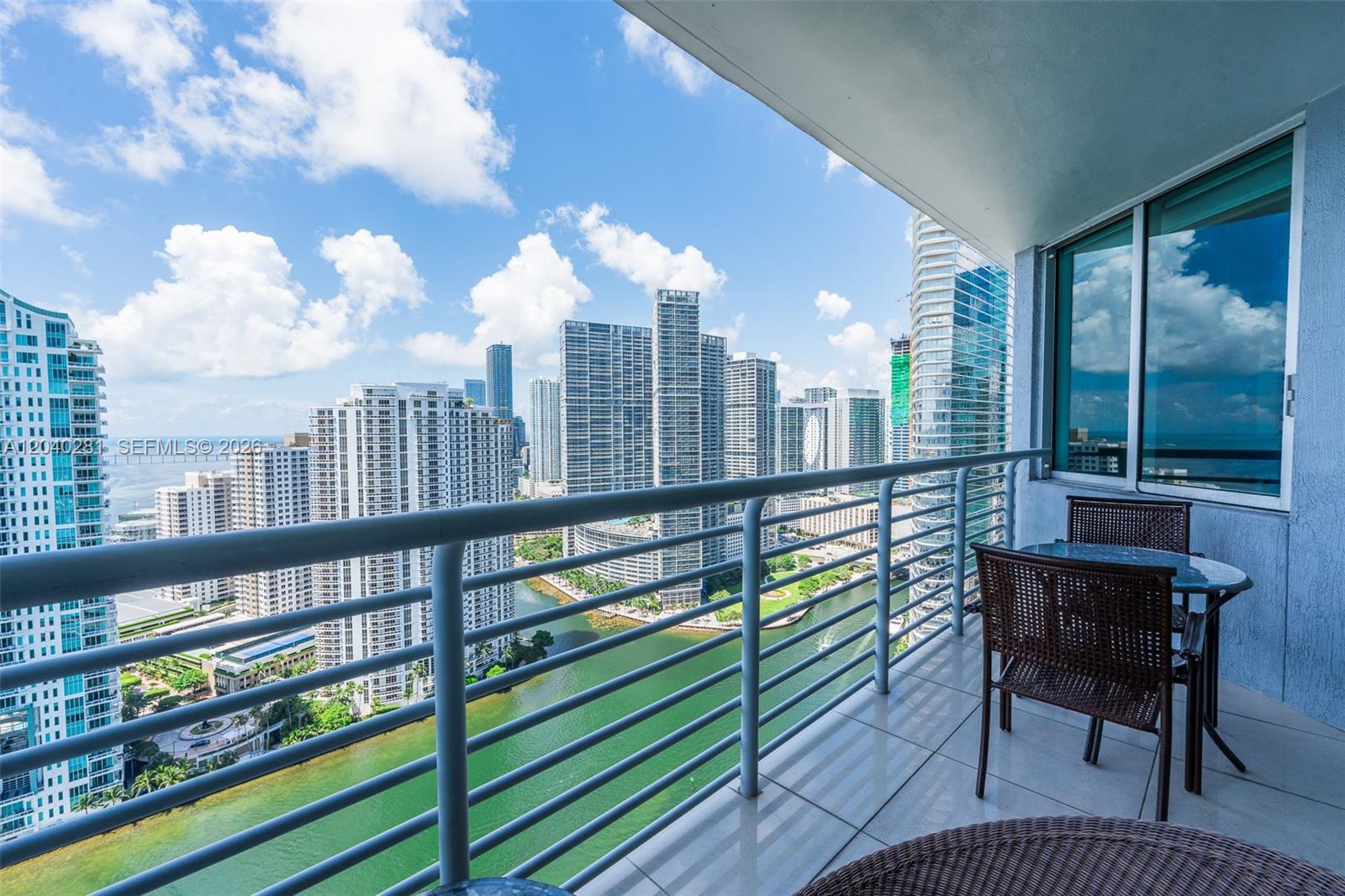 A balcony with a table and chairs overlooks a river and city skyline — 325 S Biscayne Blvd # 3821, Miami FL 33131, MIAMI, FL