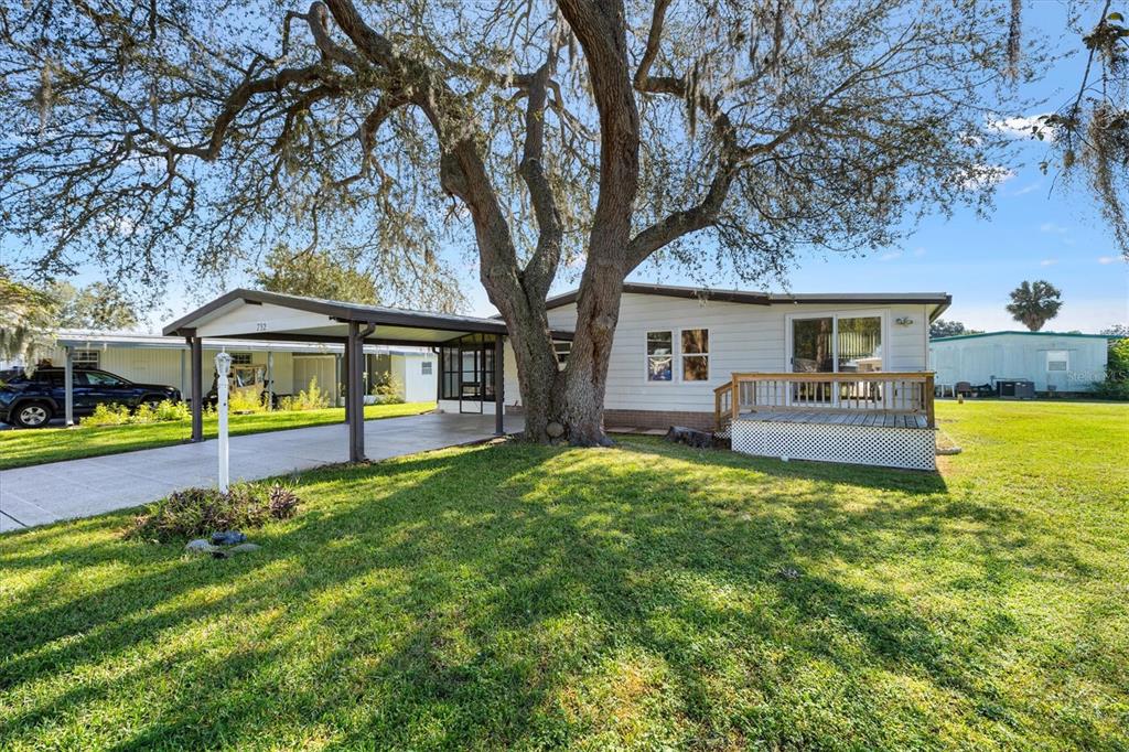 A single-story house with a carport and a wooden deck under a large oak tree — 732 ROYAL PALM AVENUE, LADY LAKE, FL
