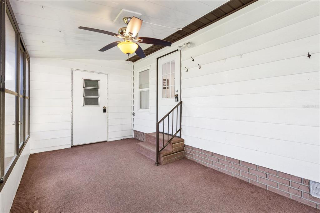 A covered porch features white horizontal siding, a ceiling fan, brown carpeting, and brick accents — 732 ROYAL PALM AVENUE, LADY LAKE, FL