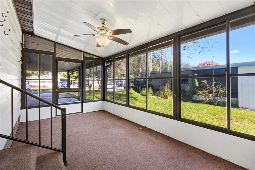 A sunroom with brown carpet, a ceiling fan, and large windows overlooking a grassy yard — 732 ROYAL PALM AVENUE, LADY LAKE, FL