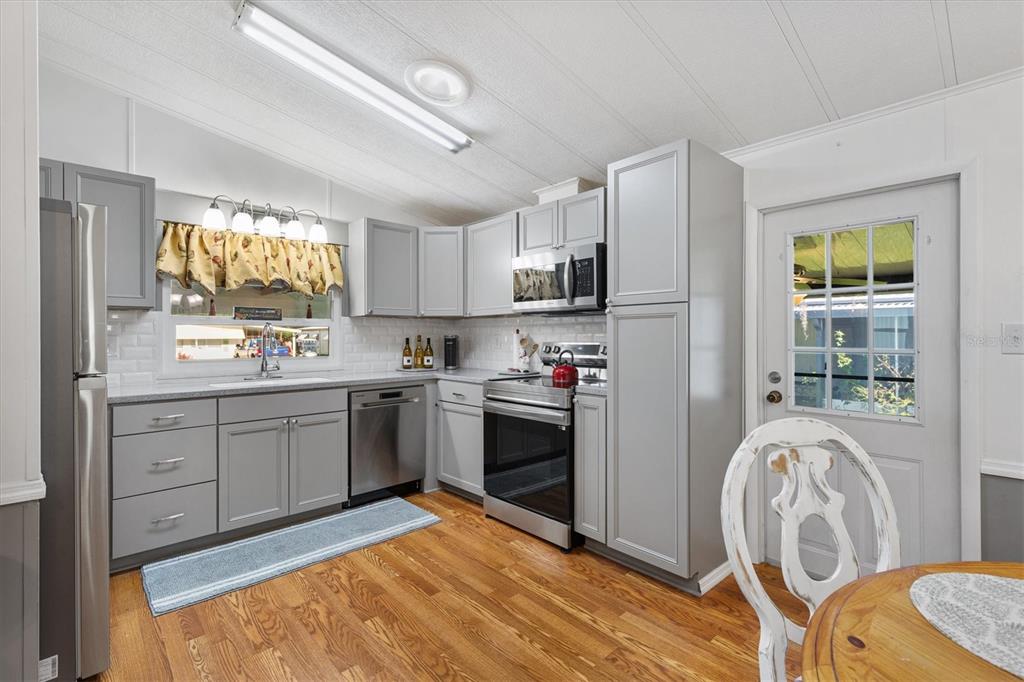 A kitchen features gray cabinets, stainless steel appliances, white subway tile backsplash, and wood flooring — 732 ROYAL PALM AVENUE, LADY LAKE, FL