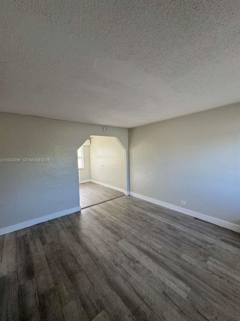 An empty room with gray wood-look flooring and a wide arched doorway to another space — RIVIERA BEACH, FL