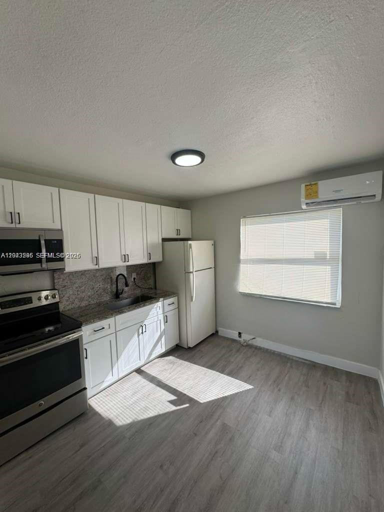 A kitchen features white cabinets, stainless steel appliances, granite countertops, and light wood-look flooring — RIVIERA BEACH, FL