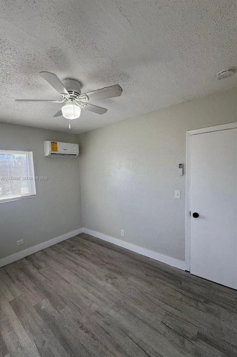 A bedroom features light gray walls, wood-look flooring, a ceiling fan, and a wall-mounted air conditioner — RIVIERA BEACH, FL