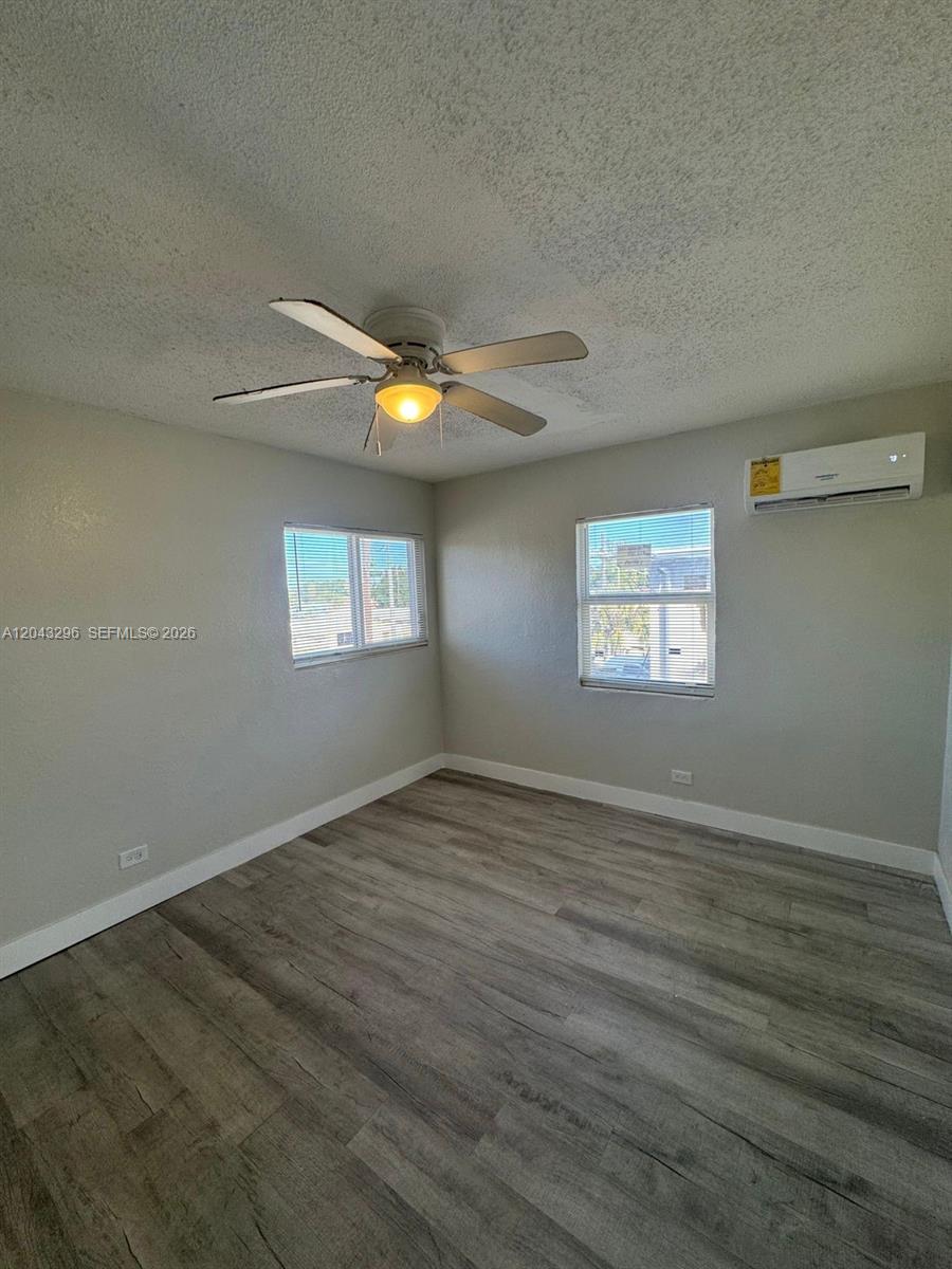 An empty bedroom features light gray walls, wood-look flooring, a ceiling fan, and a wall-mounted AC — RIVIERA BEACH, FL