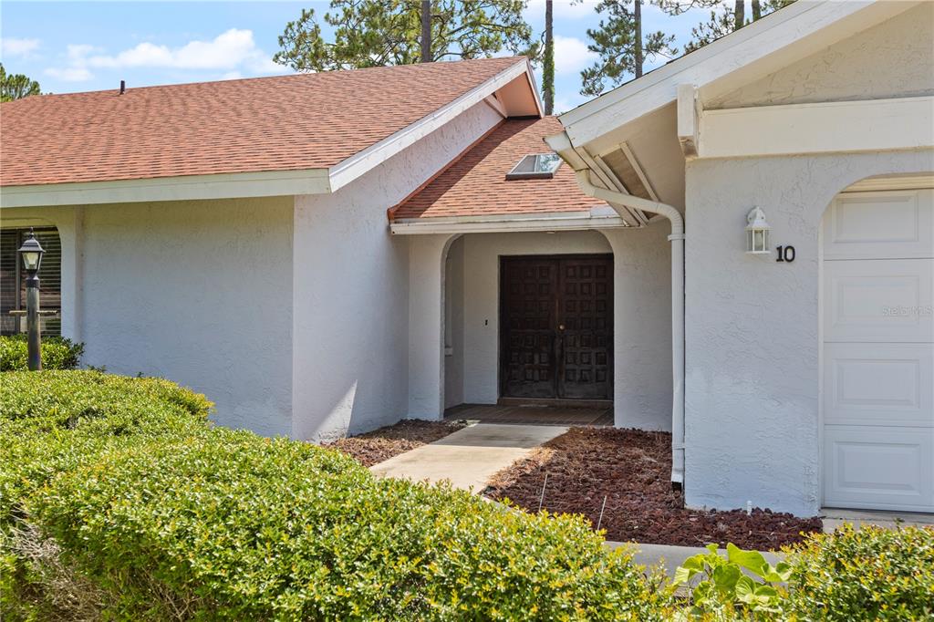 A white house exterior features a brown shingled roof, double front doors, and a skylight — 10 VILLAGE LANE, PALM COAST, FL