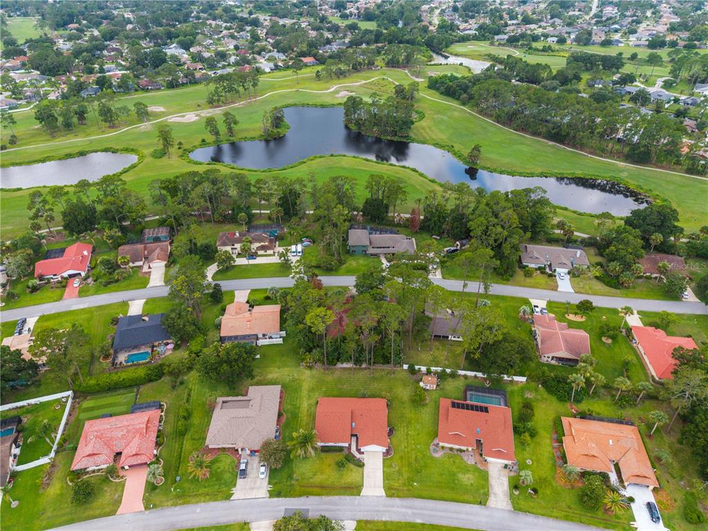 An aerial view shows suburban houses with red-tiled roofs bordering a golf course and lake — 10 VILLAGE LANE, PALM COAST, FL